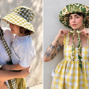 May include: Two bucket hats with a green and white gingham pattern featuring long fabric ties. A third wide-brimmed hat features a green and white floral paisley print with long ties, worn with a yellow and white gingham dress with ruffles.
