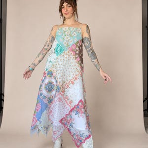 May include: A sleeveless midi dress featuring a patchwork design composed of various floral-patterned fabrics in shades of light blue, white, pink, and brown. The garment has a square neckline, thin shoulder straps, and an asymmetrical hemline.