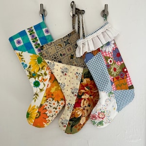 May include: Three vintage patchwork Christmas stockings with floral and geometric patterns in shades of blue, green, yellow, orange, red, and white.