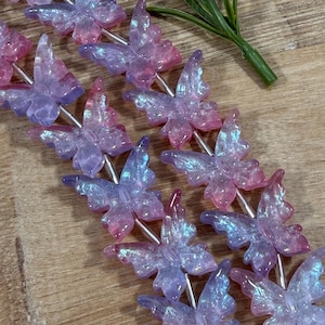 May include: Two strands of iridescent butterfly-shaped beads featuring a gradient of translucent purple and pink hues. Each bead has a textured, crackled surface finish that catches the light, creating a shimmering effect along the silver-toned string.