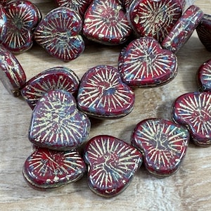 May include: Close-up of heart-shaped beads in shades of red and gold. The beads have a textured, metallic finish with a radial design. These beads are ideal for jewelry making and crafting projects.