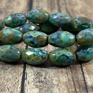 May include: A strand of oval-shaped glass beads with a mottled green and brown color pattern. The beads have a faceted surface.