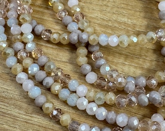May include: Close-up of several strands of beaded necklaces. The beads are in shades of light pink, beige, and gray. The beads have a faceted, crystal-like appearance, reflecting light. The necklaces are arranged in a layered, cascading style.