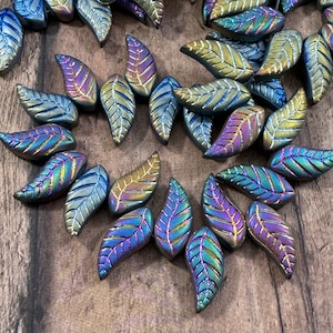 May include: A collection of iridescent leaf-shaped beads. The beads have a metallic sheen with colors ranging from blue and purple to gold and green. Each bead features detailed veining.