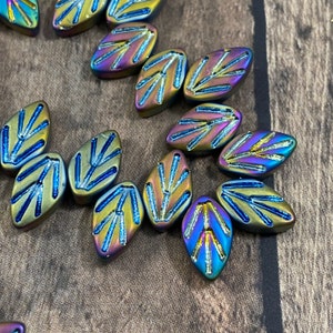 May include: A collection of iridescent glass beads in the shape of leaves with a blue and gold design. The beads have a metallic finish and are perfect for jewelry making.