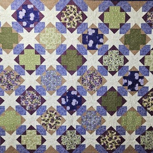 May include: A handmade quilt with a repeating pattern of squares and crosses. The quilt features a color palette of white, blue, green, and purple. The squares are filled with floral and polka dot patterns.