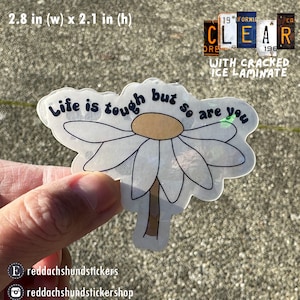 May include: A clear sticker with a white daisy and the text "Life is tough but so are you". The sticker is 2.8 inches wide and 2.1 inches tall.