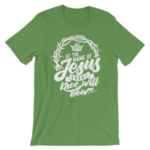 May include: Green t-shirt with a white graphic design featuring a crown of thorns, the words "At the name of Jesus every knee will bow", and the scripture reference "Philippians 2:10".