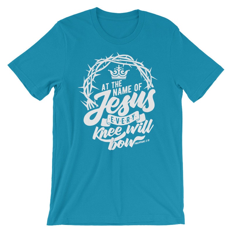 May include: A turquoise blue t-shirt with a white graphic design. The graphic features a crown of thorns, a crown, and the text "At the name of Jesus every knee will bow Philippians 2:10".
