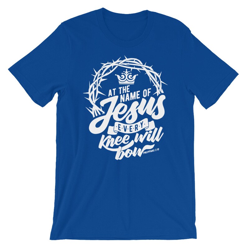 May include: A royal blue t-shirt with a white graphic design. The graphic features a crown, a crown of thorns, and the text "At the name of Jesus every knee will bow Philippians 2:10".