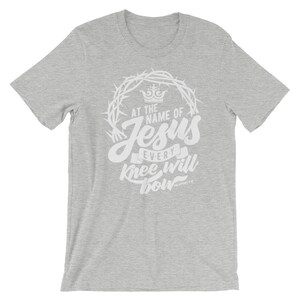 May include: Gray t-shirt with a white graphic design. The graphic features a crown, thorns, and the text "At the name of Jesus every knee will bow" with the scripture reference "Philippians 2:10".