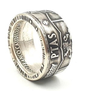 Op de afbeelding: Zilveren ring gemaakt van een vintage Spaanse munt met de tekst "Francisco Franco Caudillo" en "Pitas" aan de zijkant. De ring heeft een versleten, antieke uitstraling.
