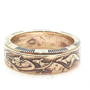 Pode incluir: Um anel de ouro feito com uma moeda australiana que apresenta cangurus. O anel é uma banda com uma borda elevada e os cangurus estão em relevo na banda.