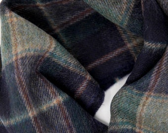 May include: A close-up of a soft, green, brown, and black plaid scarf. The scarf is folded and the fabric is textured.