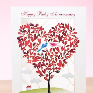 Può includere: Biglietto di anniversario fatto a mano con un design ad albero a forma di cuore. L'albero presenta foglie rosse e piccoli fiori, con due uccelli appollaiati sui suoi rami. Il biglietto recita "Happy Ruby Anniversary".