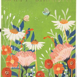 Peut inclure: Carte de vœux avec l'inscription dorée "HAPPY BIRTHDAY". Le fond vert présente un motif floral avec des marguerites blanches, des fleurs orange et des papillons. La carte porte également le logo Dreamy London.