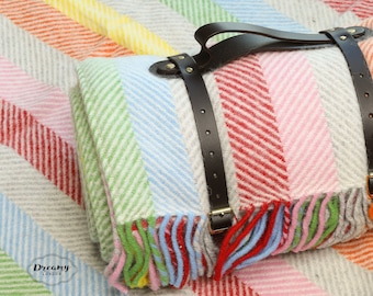 May include: A rainbow striped blanket with leather straps, folded and rolled up. The blanket has a fringe border and is made of a soft, woven fabric.