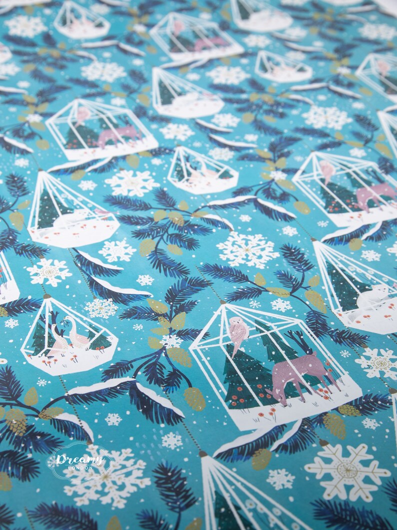 May include: Blue wrapping paper with a repeating pattern of white birdcages filled with small trees, birds, and deer. The background is a light blue with white snowflakes.