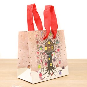May include: A red and white gift bag with a winter scene featuring a tree house and a snowy landscape. The bag has red ribbon handles and the text "Dreamy London" is printed on the bottom.