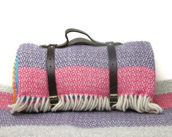 May include: A rolled up striped blanket with a leather handle and buckles. The blanket is folded and has a fringe on the edges. The blanket is on a striped surface.
