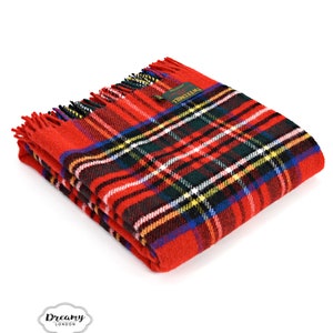 May include: Red and black tartan throw blanket with fringed edges. The blanket is folded in half and has a small label that says "Tweedmill" on it.