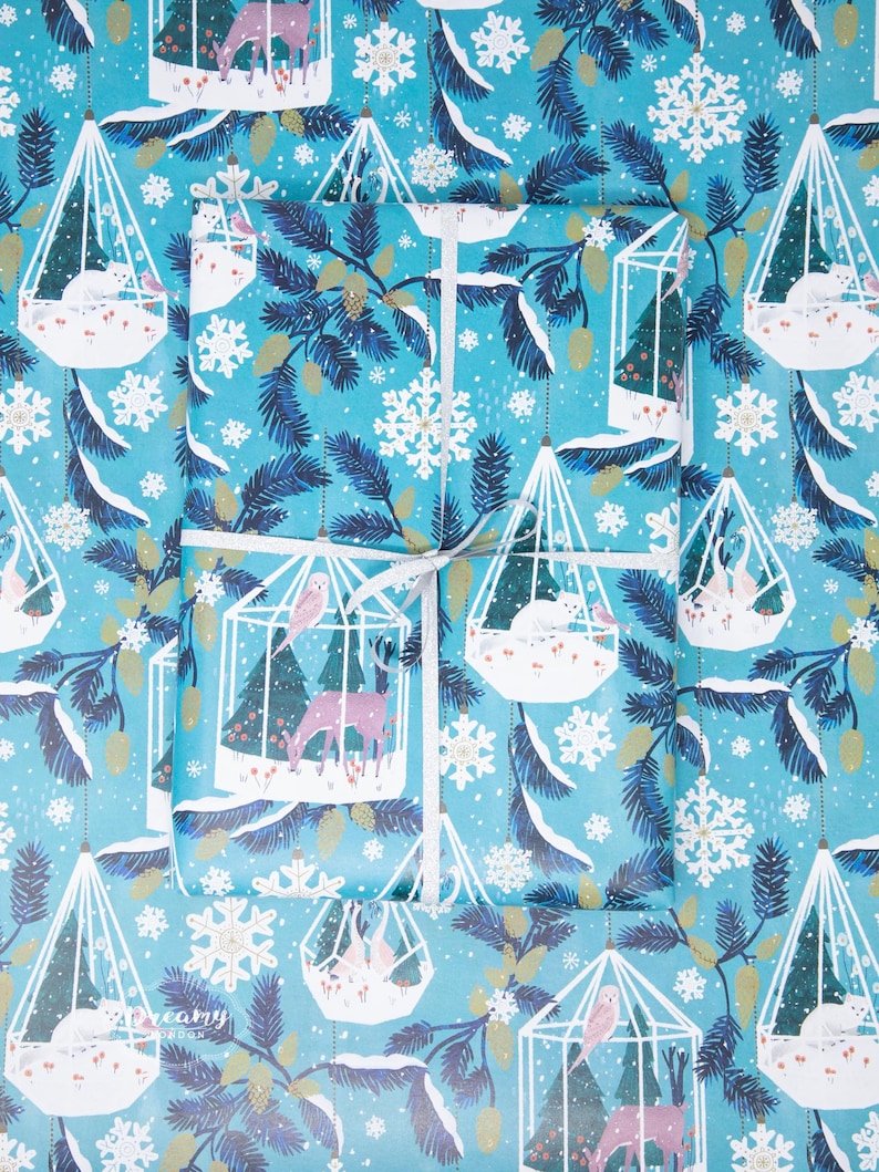 May include: Blue wrapping paper with a repeating pattern of white cages containing birds, deer, and snowflakes. The cages are suspended from a string and are surrounded by pine branches.
