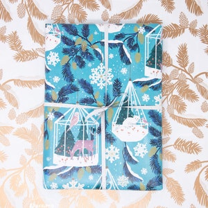 May include: Blue and white wrapping paper with a wintery design featuring birds, deer, and snowflakes. The paper is wrapped around a gift box with a white ribbon.