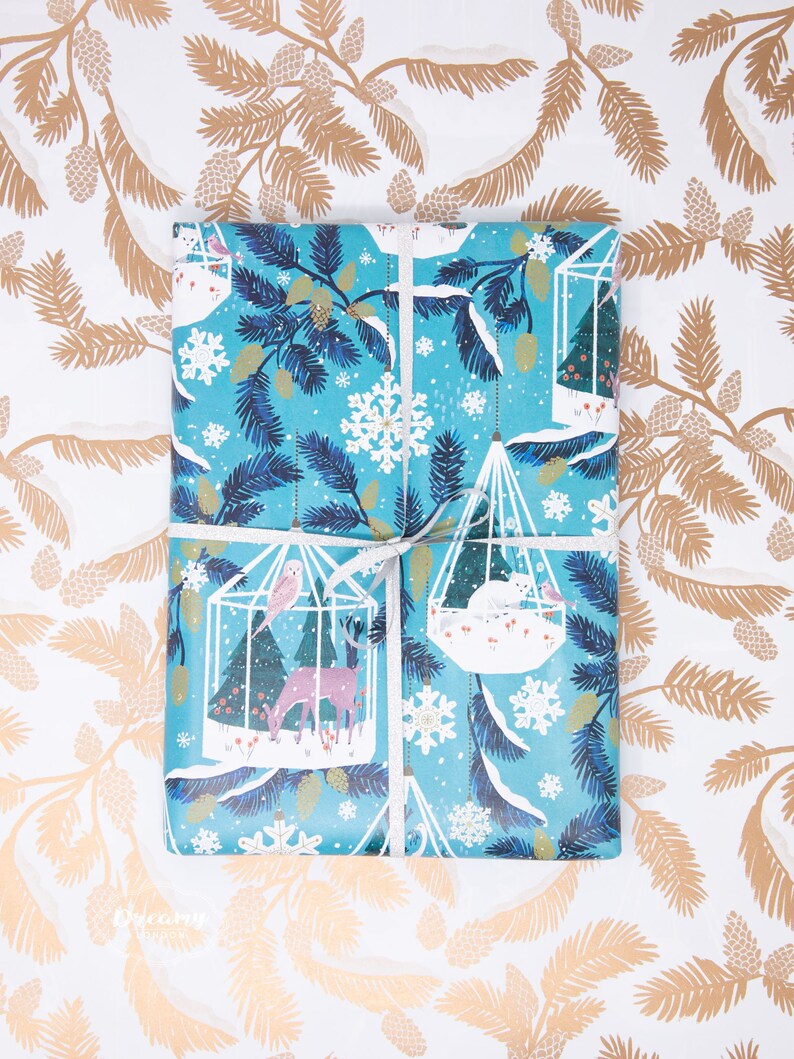 May include: Blue and white wrapping paper with a wintery design featuring birds, deer, and snowflakes. The paper is wrapped around a gift box with a white ribbon.