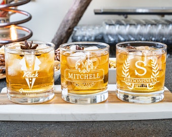 Könnte beinhalten: Drei personalisierte Whiskeygläser mit verschiedenen Designs. Das erste Glas hat einen Smoking mit dem Namen "Rick" und dem Text "Groomsman 9.23.2023". Das zweite Glas hat ein Wappen mit dem Namen "Mitchell" und dem Text "Groomsman". Das dritte Glas hat einen Kranz mit dem Buchstaben "S" und dem Text "Groomsman 10.27.22".