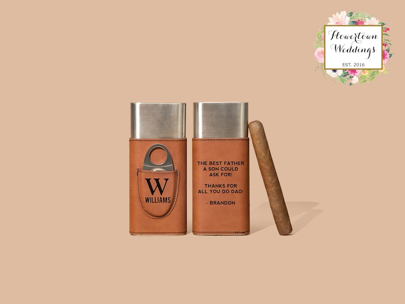 May include: Two brown leather cigar cases with a silver metal interior. One case has a cigar cutter and the initials "W" and "WILLIAMS" engraved on the front. The other case has the text "THE BEST FATHER A SON COULD ASK FOR! THANKS FOR ALL YOU DO DADI - BRANDON" engraved on the front. A brown cigar is lying on the table next to the cases.