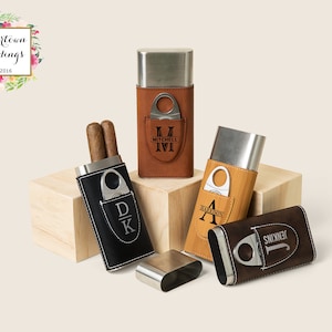 May include: Four personalized cigar cases with a built-in cutter. The cases are made of metal and leather and come in brown, black, and tan. The cases are engraved with initials and names, including "Mitchell", "Harrison", "Jenkins", and "DK".