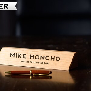 May include: A wooden desk nameplate with the text "Mike Honcho, Marketing Director" in black lettering.