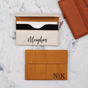 May include: Three personalized leather card holders. One is white with the name Meaghan, one is brown with the initials N|K, and one is brown with the name Seth Warner.