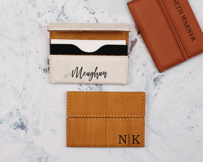 May include: Three personalized leather card holders. One is white with the name Meaghan, one is brown with the initials N|K, and one is brown with the name Seth Warner.