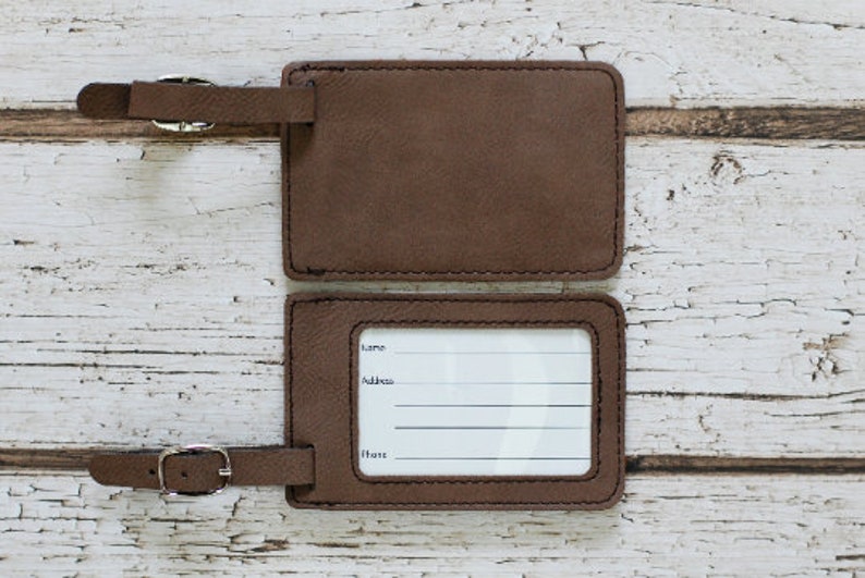 May include: Two brown leather luggage tags with white labels. The top tag is blank. The bottom tag has the words "Name", "Address", and "Phone" printed on it.