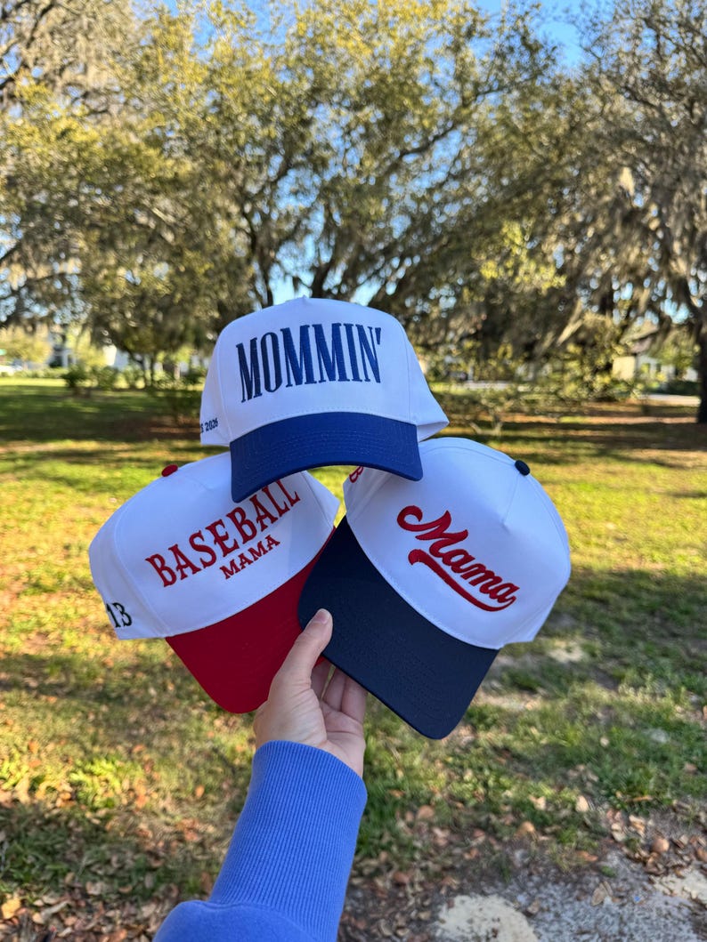 May include: Three baseball caps are displayed, each with a white crown and a coloured brim. One cap features the word "Mommin'" in blue, another says "Baseball Mama" with the number 13, and the third says "Mama" in red.