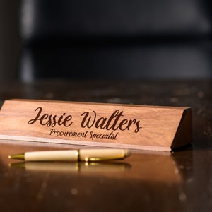 May include: A wooden desk nameplate with the text "Jessie Walters Procurement Specialist" engraved in a cursive font.