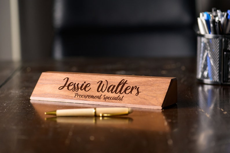 May include: A wooden desk nameplate with the text "Jessie Walters Procurement Specialist" engraved in a cursive font.
