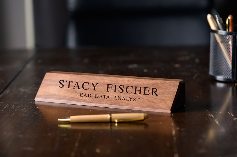 May include: A wooden desk nameplate with the text "Stacy Fischer, Lead Data Analyst" engraved in black lettering.