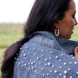 May include: A blue denim jacket with white pearl embellishments and the date "04.18.2026" embroidered on the collar.