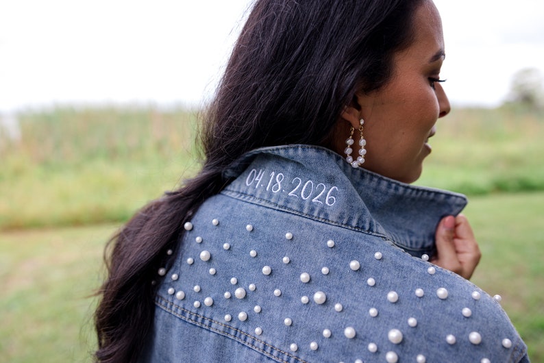 May include: A blue denim jacket with white pearl embellishments and the date "04.18.2026" embroidered on the collar.