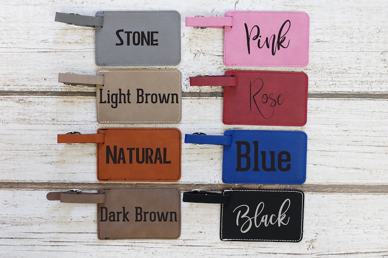 May include: Eight leather luggage tags in various colours with text. The colours are stone, light brown, natural, dark brown, pink, rose, blue, and black. The text on the tags is the colour name.