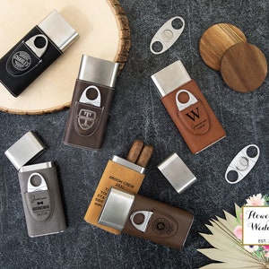 May include: A set of six personalized cigar cases with a built-in cutter. The cases are made of brown, black, and gray leather with silver metal accents. The cases are engraved with various names and messages, including "Groom Crew 2022", "Best Man", and "Groomsman".