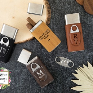 May include: Four different cigar cases with a built-in cutter. The cases are made of leather and wood and have different engravings. One case has the text "You are finer than a Cuban cigar" engraved on it. Another case has the initials "RT" engraved on it. The third case has the initial "M" engraved on it. The fourth case has the initial "T" engraved on it.