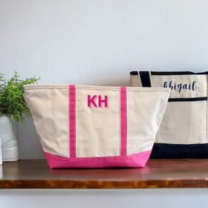 May include: Two canvas tote bags with pink trim. The bag on the left has the initials "KH" embroidered on the front in pink. The bag on the right has the name "Abigail" embroidered on the front in navy blue.