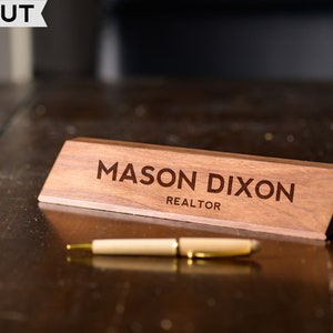 May include: A wooden desk nameplate with the text "MASON DIXON REALTOR" engraved on it. The nameplate is on a dark wood desk.