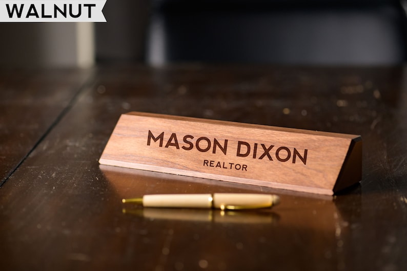 May include: A wooden desk nameplate with the text "MASON DIXON REALTOR" engraved on it. The nameplate is on a dark wood desk.