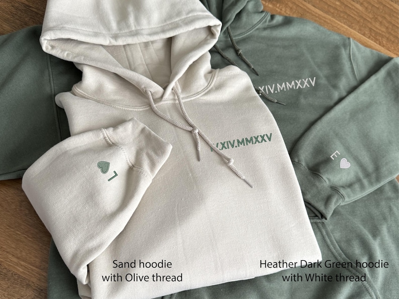 May include: Three hooded sweatshirts in sand and heather dark green. The sand hoodie has olive thread embroidery, including a heart and the number 7 on the sleeve. The dark green hoodie has white thread embroidery with the roman numerals XIV.MMXXV.
