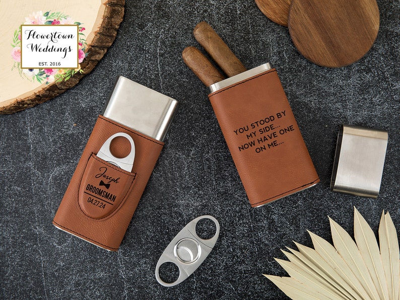 May include: Two brown leather cigar cases with silver metal inserts. One case has the text "You stood by my side... Now have one on me..." engraved on the front. The other case has the text "Joseph Groomman 0427.24" engraved on the front. A silver cigar cutter is also pictured.