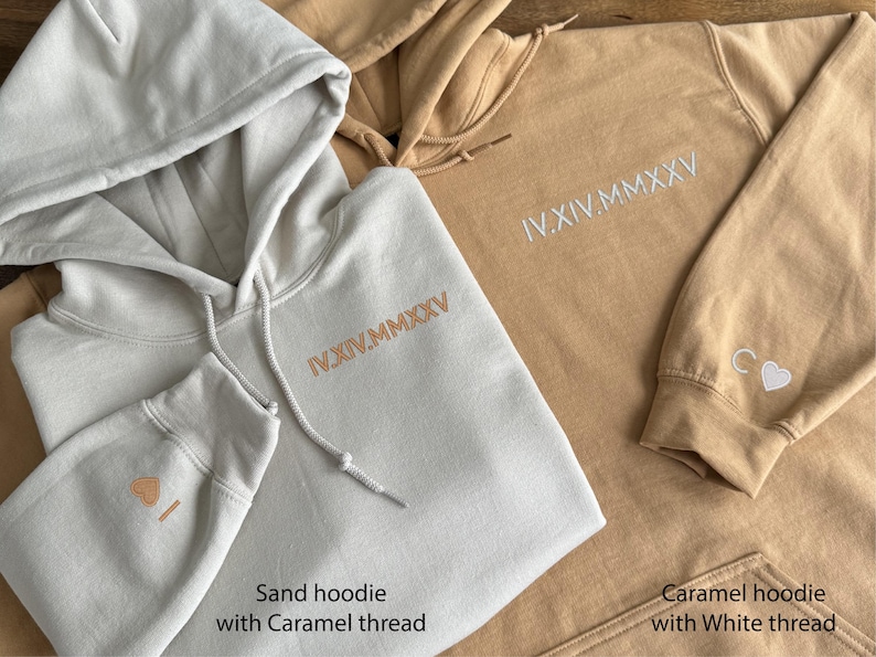 May include: Close-up of two hoodies, one sand-colored and one caramel-colored. Both have embroidered Roman numerals on the chest. The sand hoodie has caramel-colored thread, and the caramel hoodie has white thread. The sand hoodie has a small embroidered design on the sleeve.